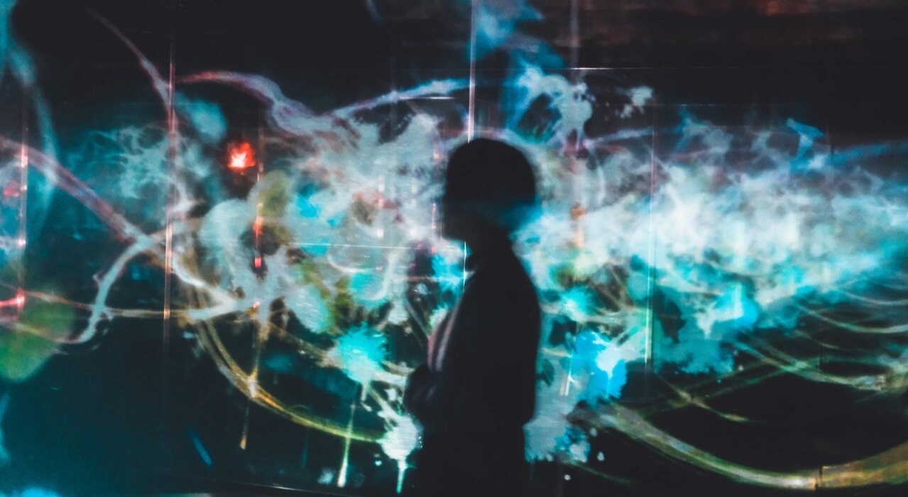 A silhouette of a person standing before glowing digital artwork showing a cloud of connected splashes.