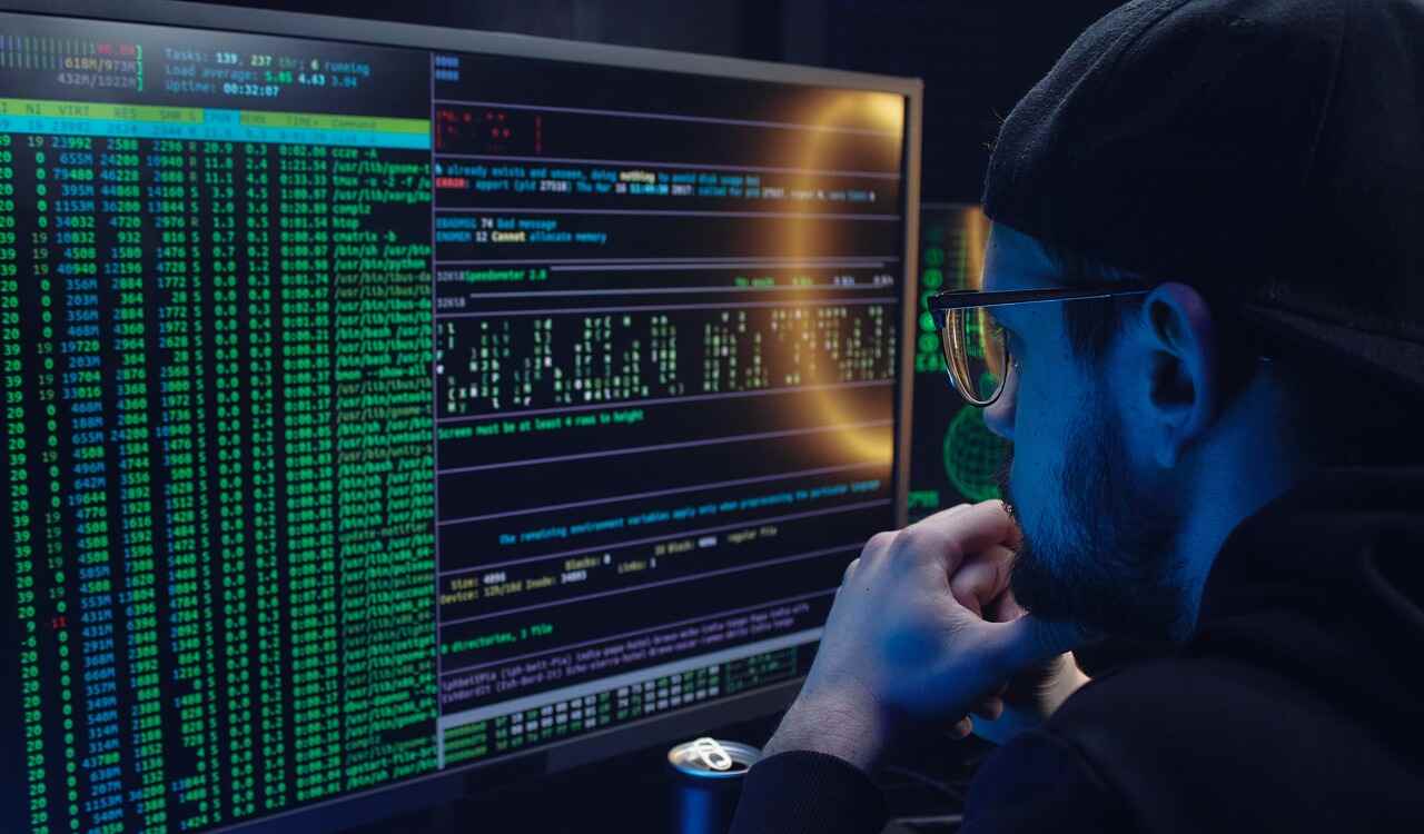 A man in a dark room inspects a computer screen covered with code.